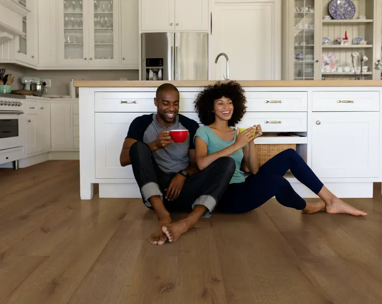 Smiling couple drinking coffee while sitting on warm oak wood-look vinyl kitchen floors.