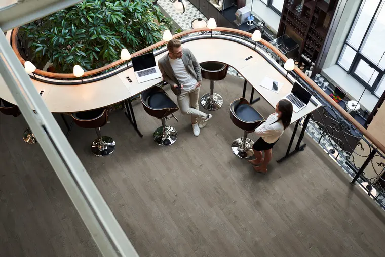 Overhead view of a modern co-working lounge with curved counter seating and gray wood-look vinyl floors.