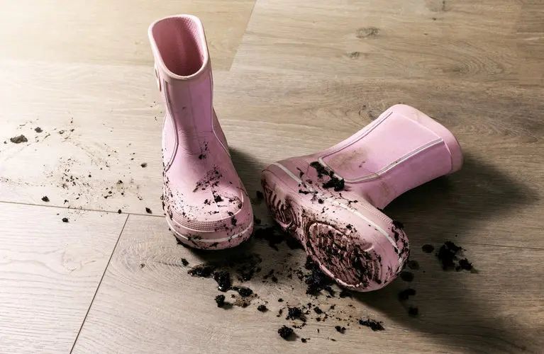 Muddy pink rain boots resting on light wood-look vinyl floor.