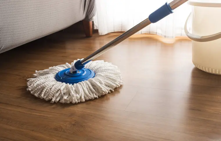 White microfiber spin mop cleaning dark wood-look vinyl flooring next to a mop bucket.